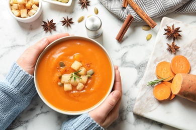 Photo of Woman with bowl of tasty sweet potato soup at table, top view