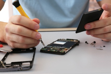 Technician repairing broken smartphone at table, closeup