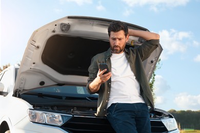 Upset man using smartphone near broken car outdoors, low angle view