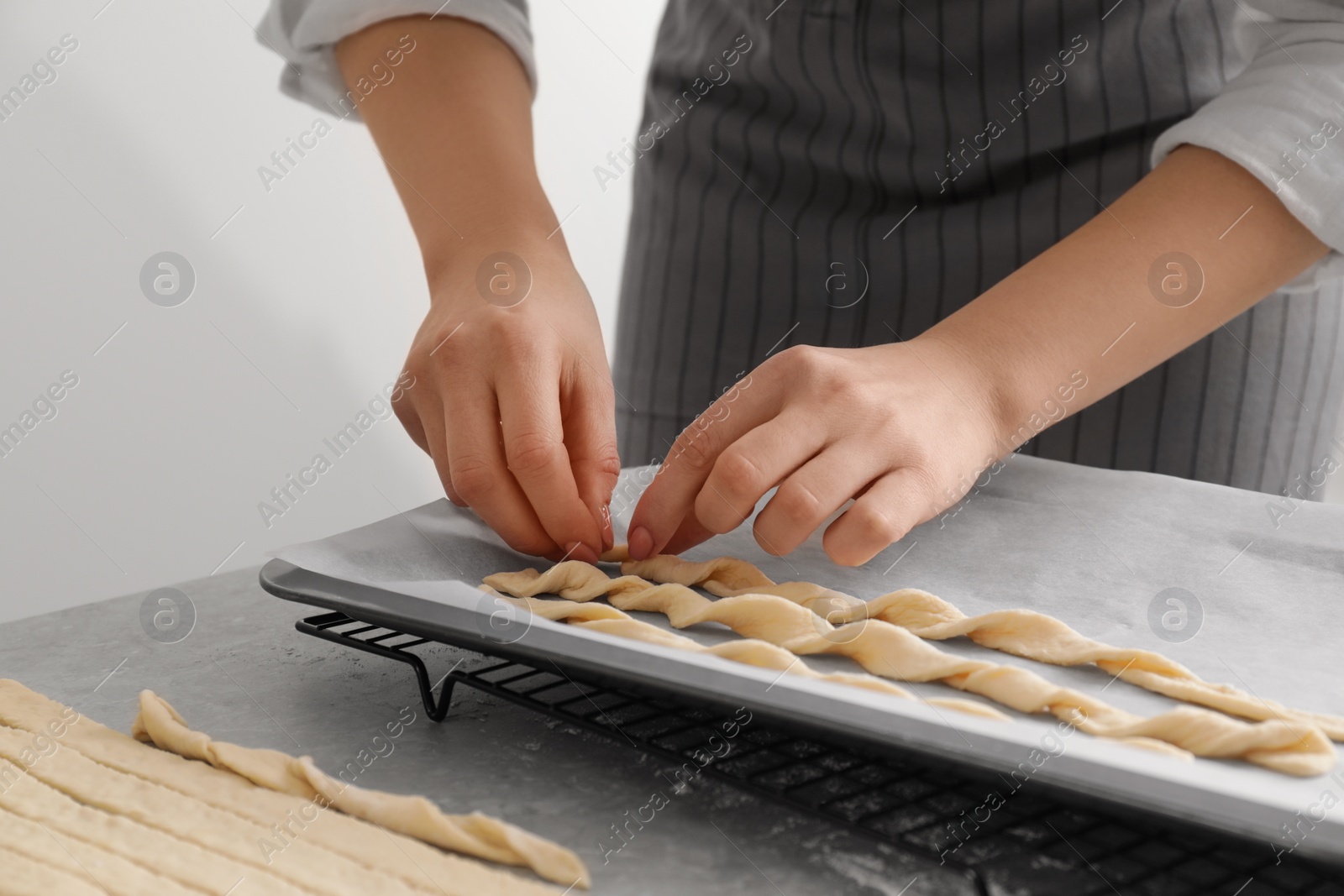 Photo of Woman putting homemade breadsticks on baking sheet at light grey marble table, closeup. Cooking traditional grissini