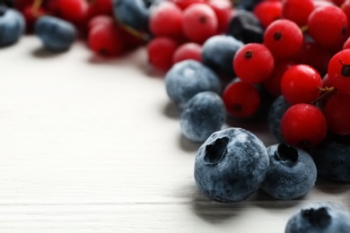 Photo of Tasty frozen blueberries and red currants on white wooden table, closeup. Space for text
