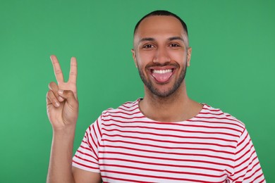 Photo of Happy young man showing his tongue and V-sign on green background