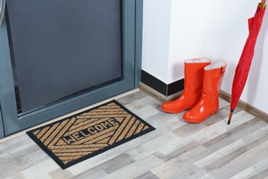 Photo of Rubber boots, umbrella and mat near door in hallway