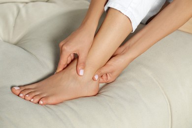 Photo of Woman rubbing sore foot on sofa, closeup