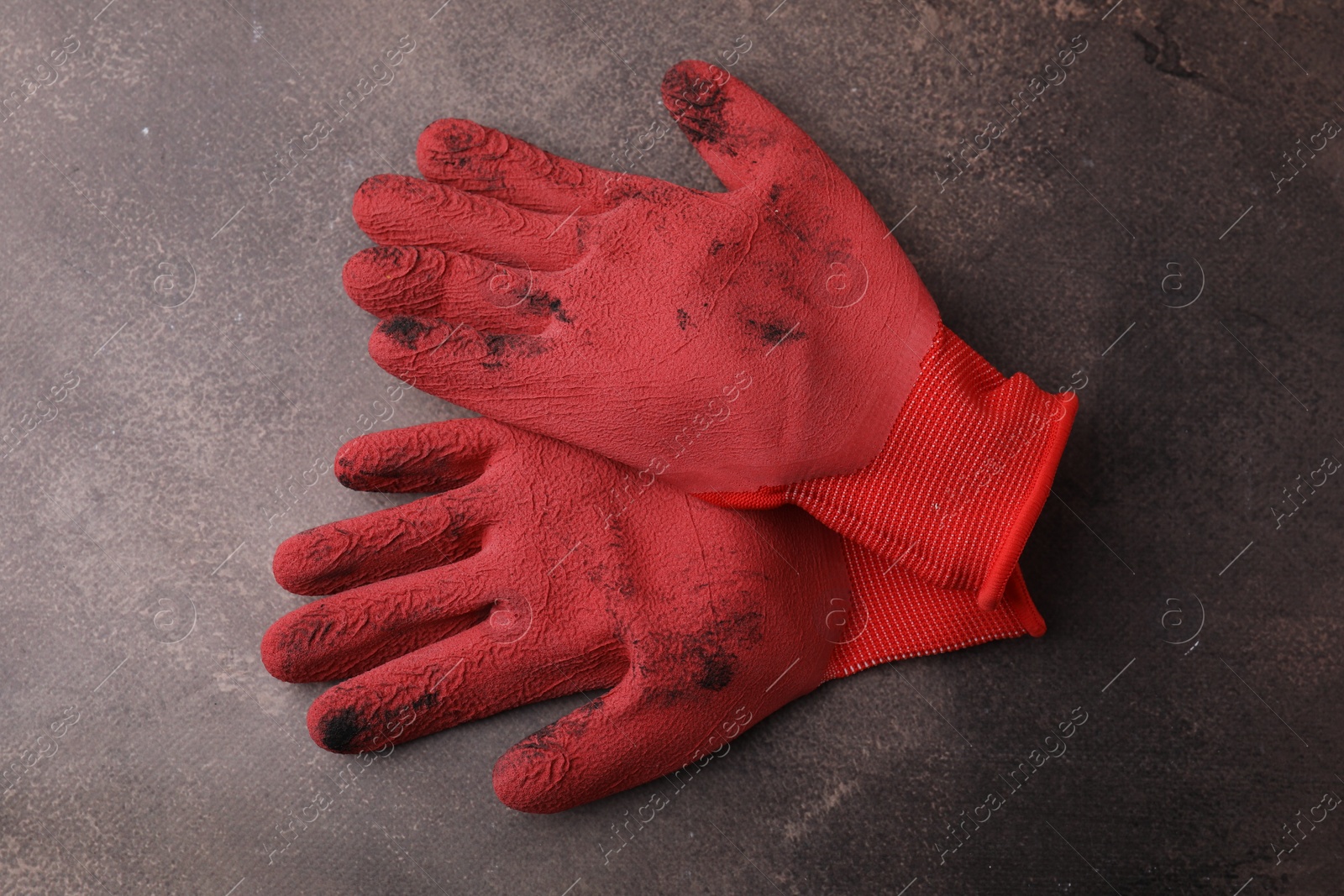 Photo of Pair of red gardening gloves on brown textured table, top view