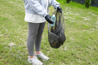 Photo of Woman with trash bag picking up plastic bottle outdoors, closeup. Recycling concept