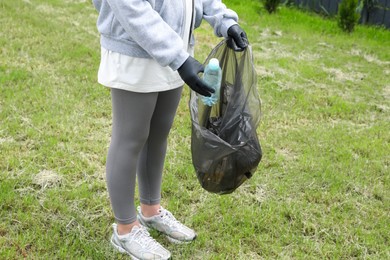 Woman with trash bag picking up plastic bottle outdoors, closeup. Recycling concept