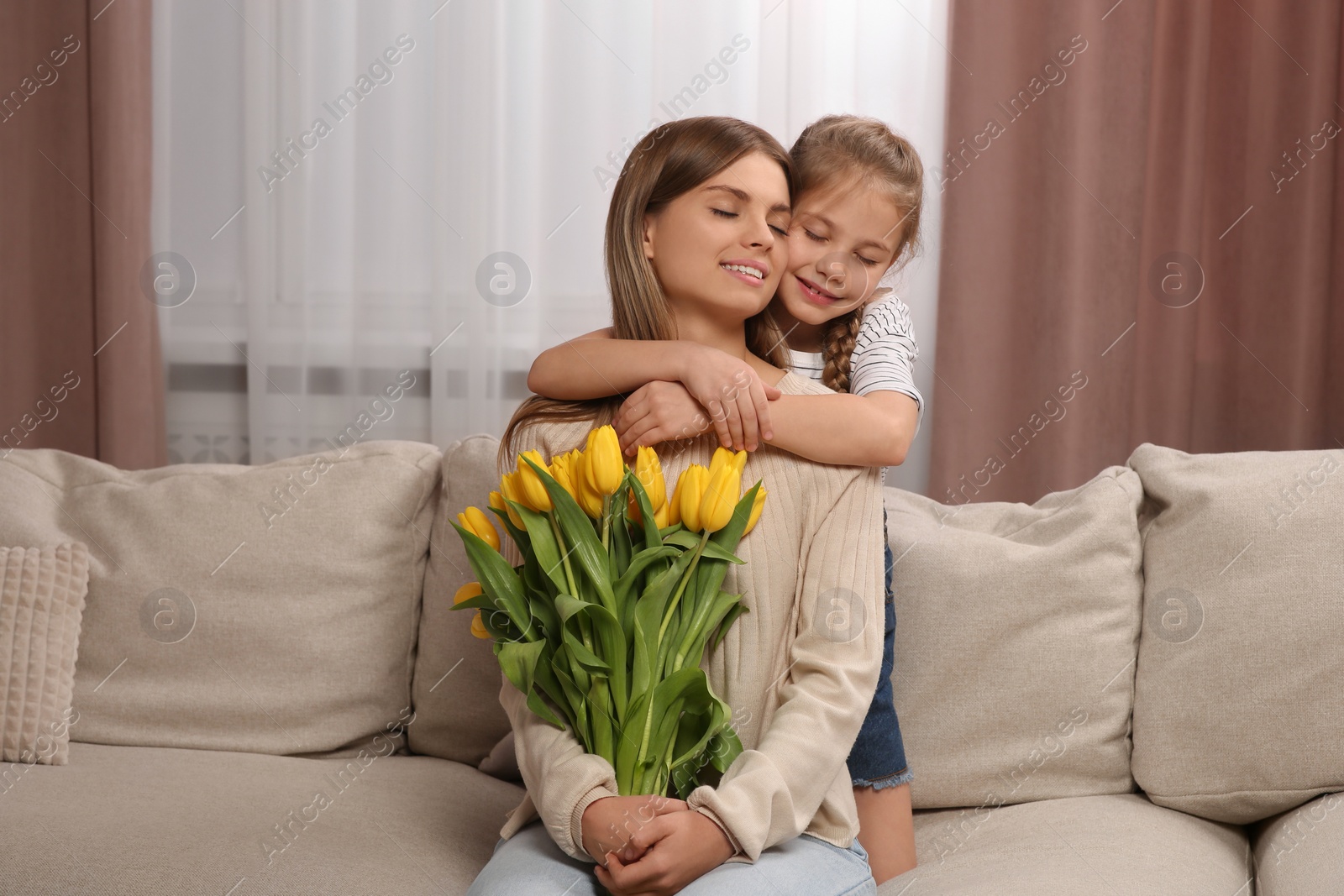 Photo of Little daughter congratulating mom with bouquet of yellow tulips at home. Happy Mother's Day