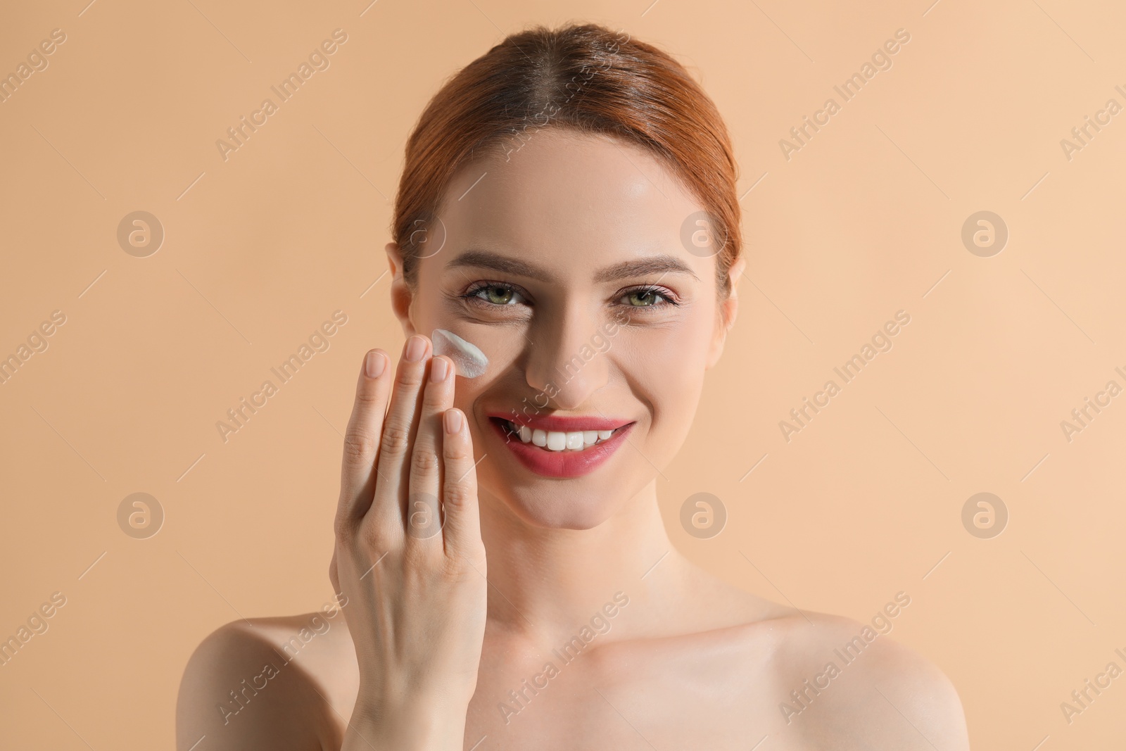 Photo of Beautiful young woman with sun protection cream on her face against beige background