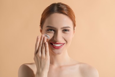 Photo of Beautiful young woman with sun protection cream on her face against beige background