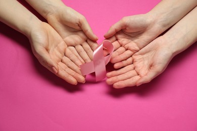 Women holding pink ribbon on color background, top view. Breast cancer awareness