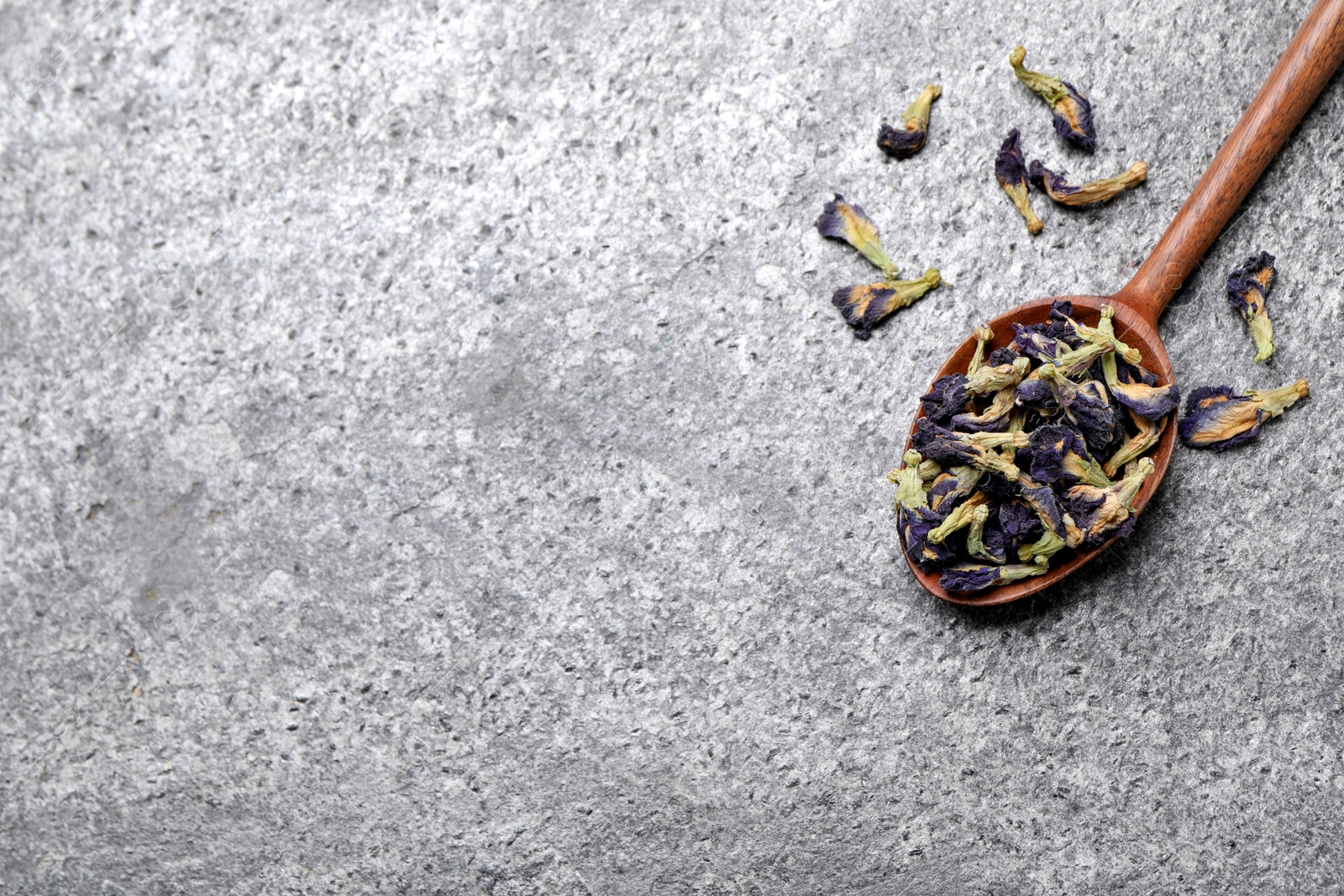 Photo of Spoon and dry organic blue Anchan on grey table, flat lay with space for text. Herbal tea