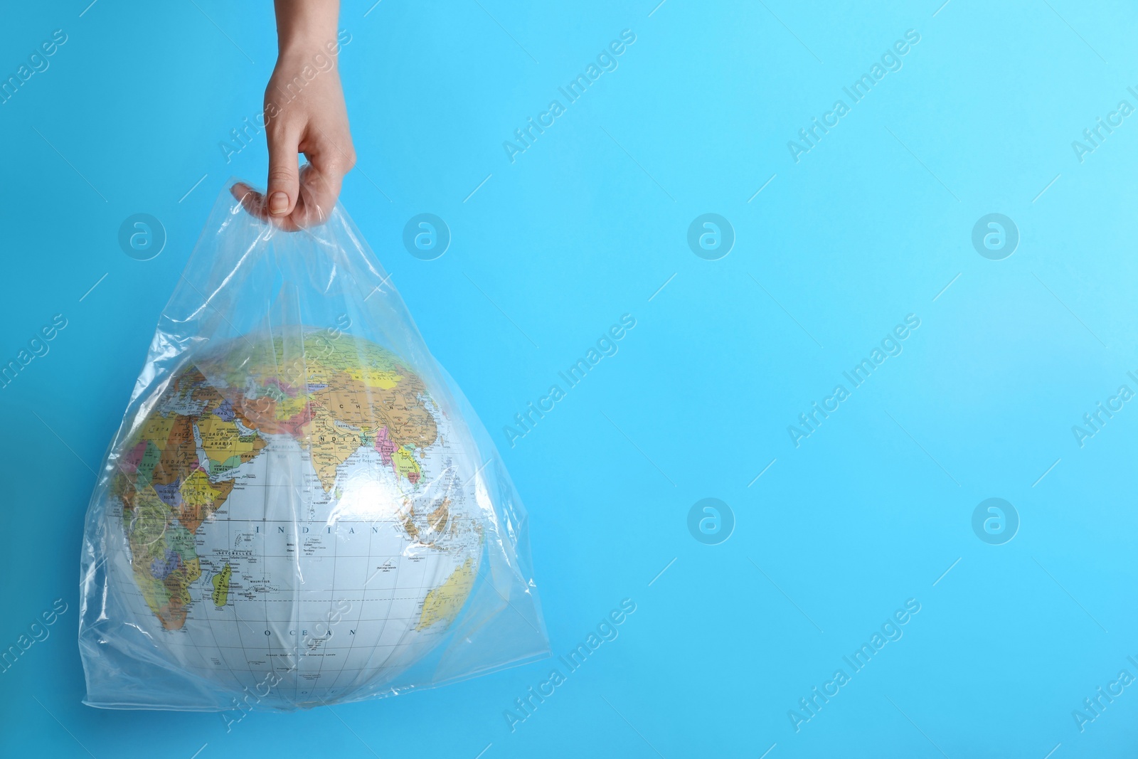 Photo of Woman holding plastic bag with globe and space for text on turquoise background, closeup. Environmental conservation