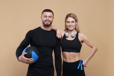 Photo of Athletic people with skipping rope, headphones and medicine ball on light brown background