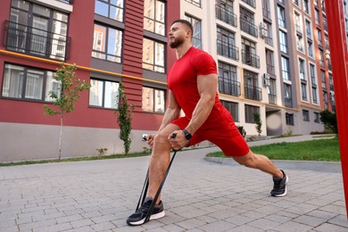 Photo of Muscular man doing exercise with elastic resistance band on sports ground, low angle view