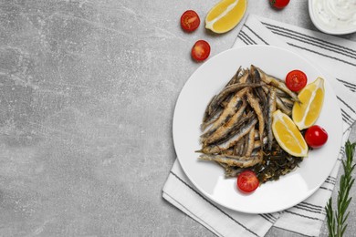 Delicious fried anchovies with cherry tomatoes and slices of lemon served on light grey table, flat lay. Space for text