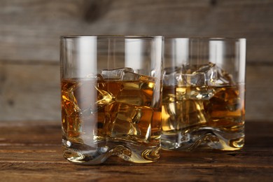 Photo of Whiskey with ice cubes in glasses on wooden table, closeup