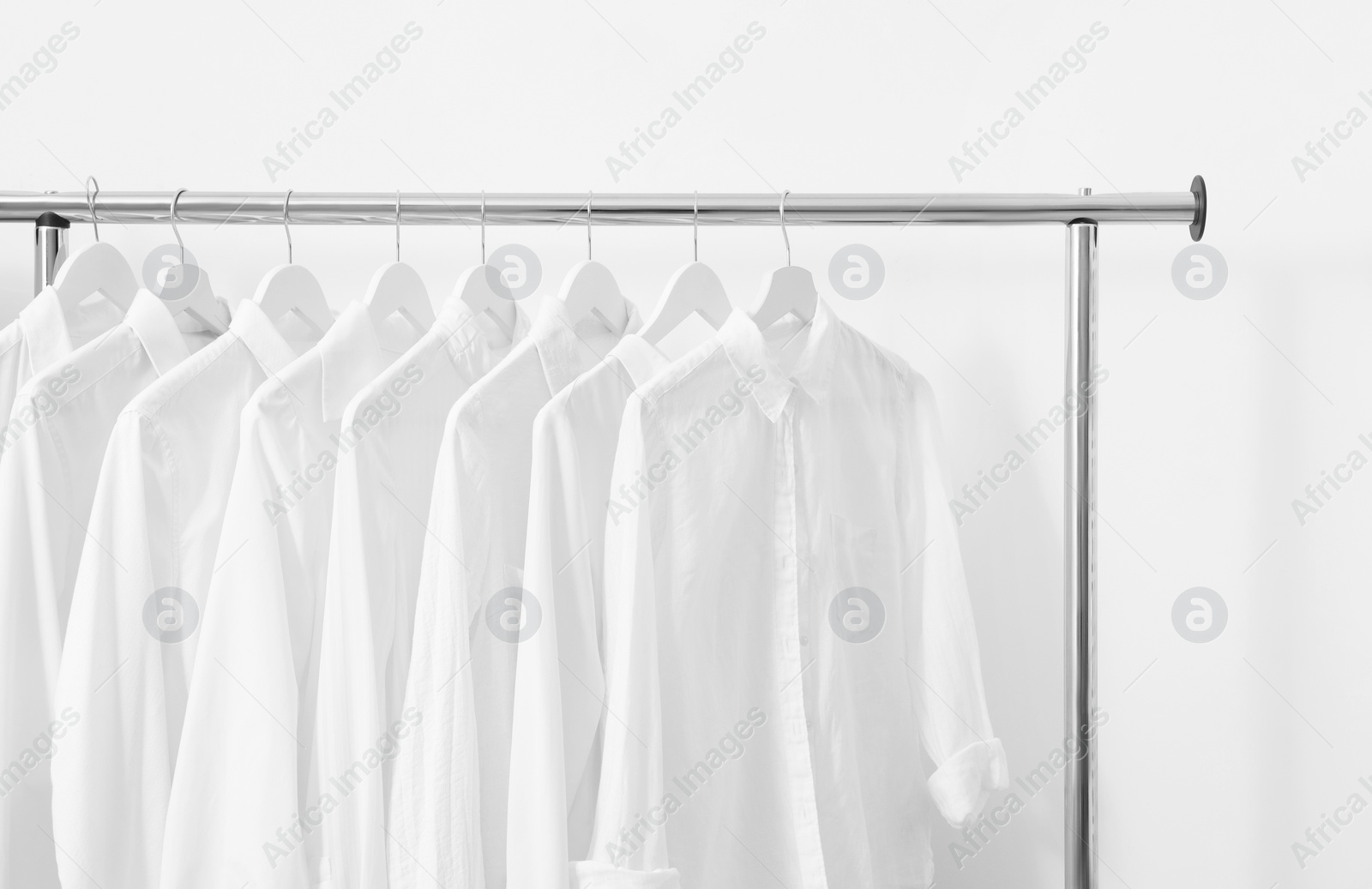 Photo of Rack with different stylish shirts near white wall. Organizing clothes