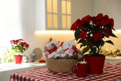 Photo of Basket with gifts for Christmas advent calendar, plant and cup of cocoa on table in kitchen