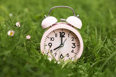 Photo of Pink alarm clock on green grass outdoors, closeup