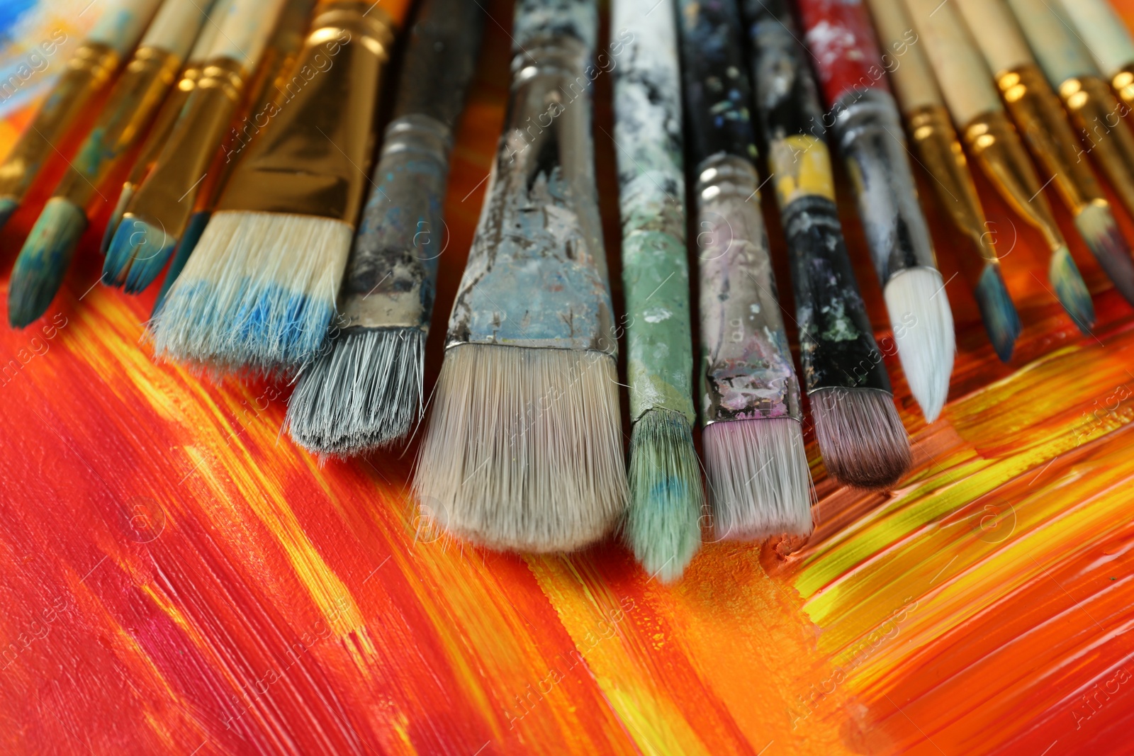 Photo of Set of different brushes on abstract colorful paint, closeup