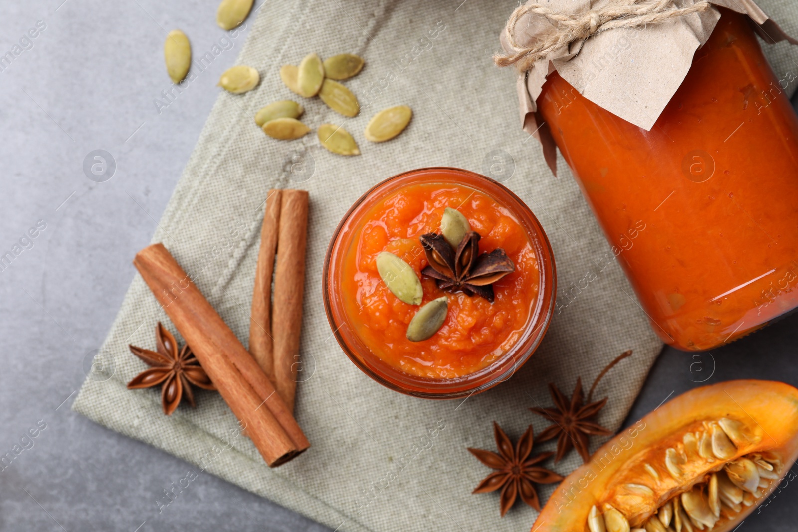 Photo of Jars of pumpkin jam, star anise, cinnamon and fresh pumpkin on grey table, flat lay