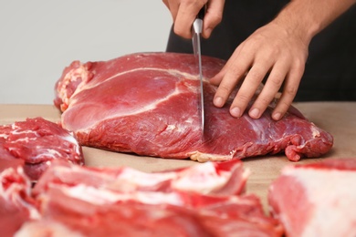 Photo of Butcher cutting fresh raw meat on counter in shop, closeup