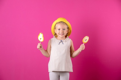 Photo of Cute little girl with candies on color background