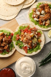 Delicious tacos with vegetables, meat and sauce on grey textured table, flat lay