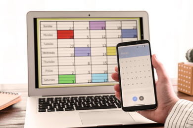 Photo of Woman holding smartphone with calendar app at table, closeup