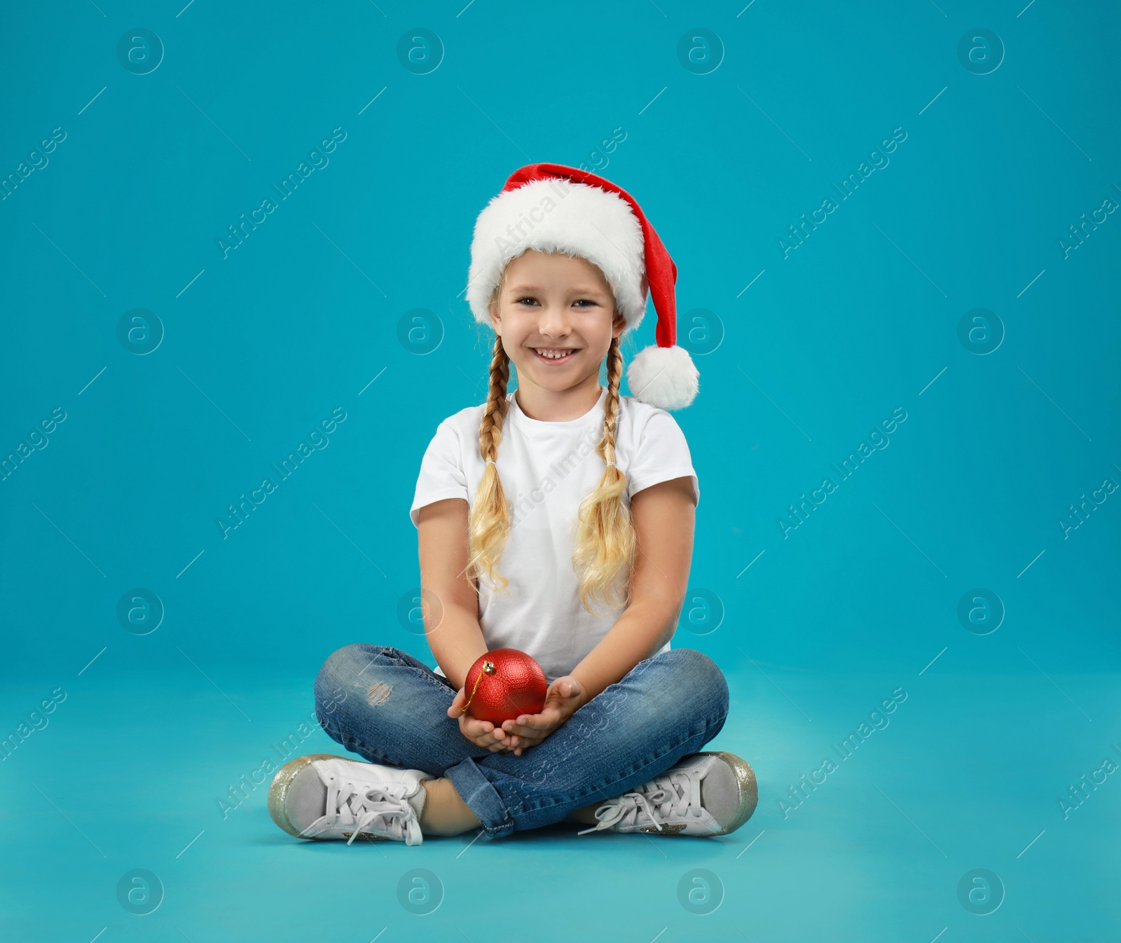 Photo of Cute little child wearing Santa hat holding Christmas decoration on blue background