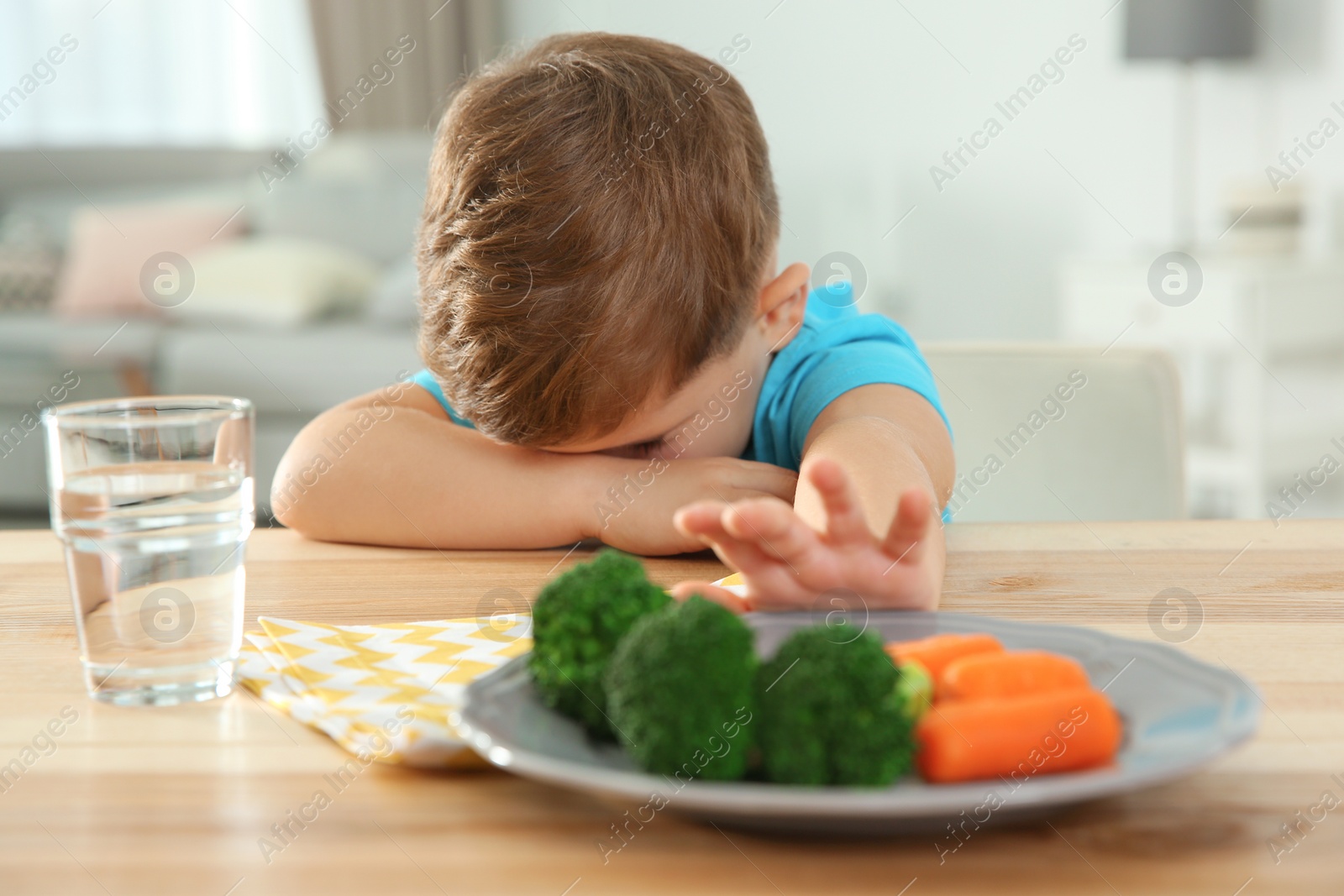 Photo of Unhappy little boy refusing to eat vegetables at table in room