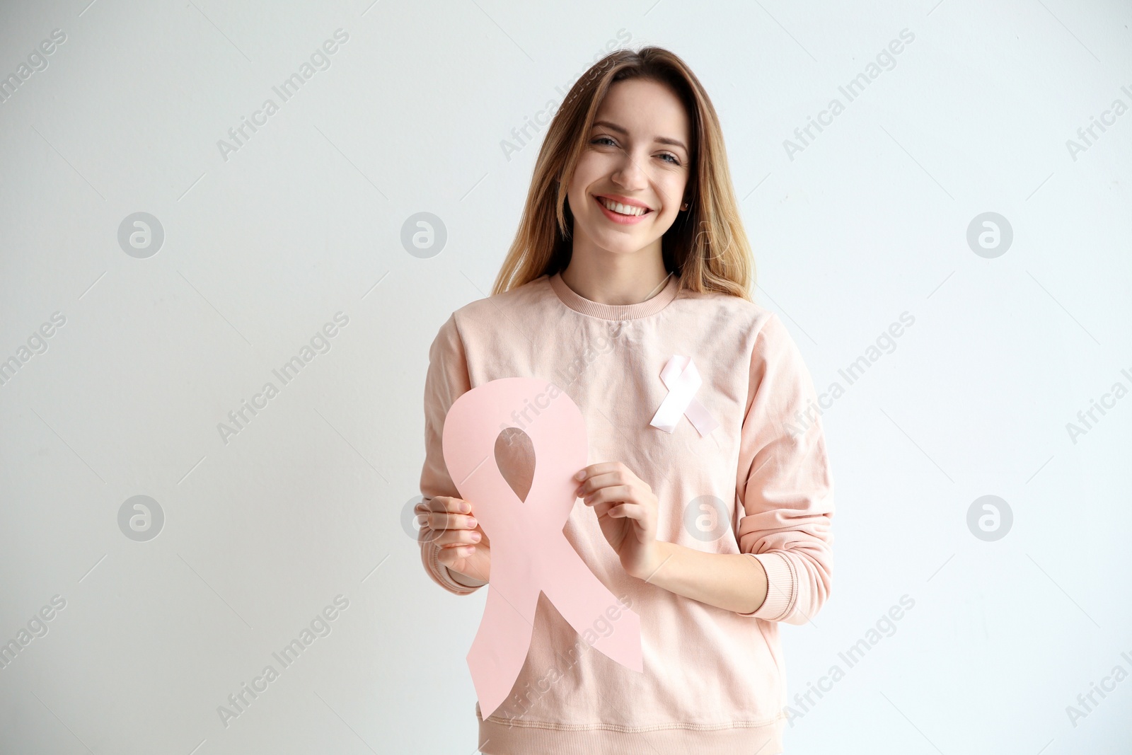 Photo of Woman holding pink paper ribbon against white background. Breast cancer awareness concept