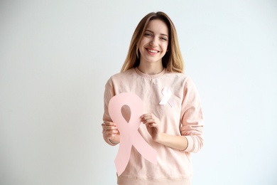 Woman holding pink paper ribbon against white background. Breast cancer awareness concept