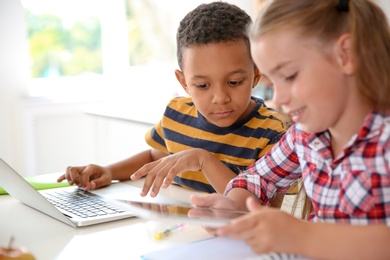 Cute little children with gadgets sitting at desk in classroom. Elementary school