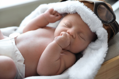 Photo of Cute newborn baby in aviator hat sleeping on blanket, closeup