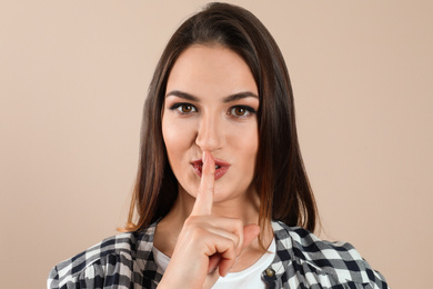 Photo of Beautiful young woman showing silence gesture on beige background