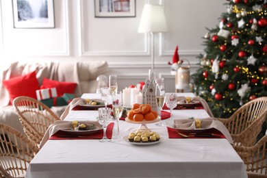 Photo of Christmas table setting with tangerines, candies and dishware in room