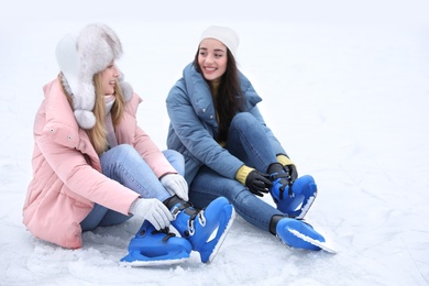 Happy women with figure skates sitting on ice rink outdoors