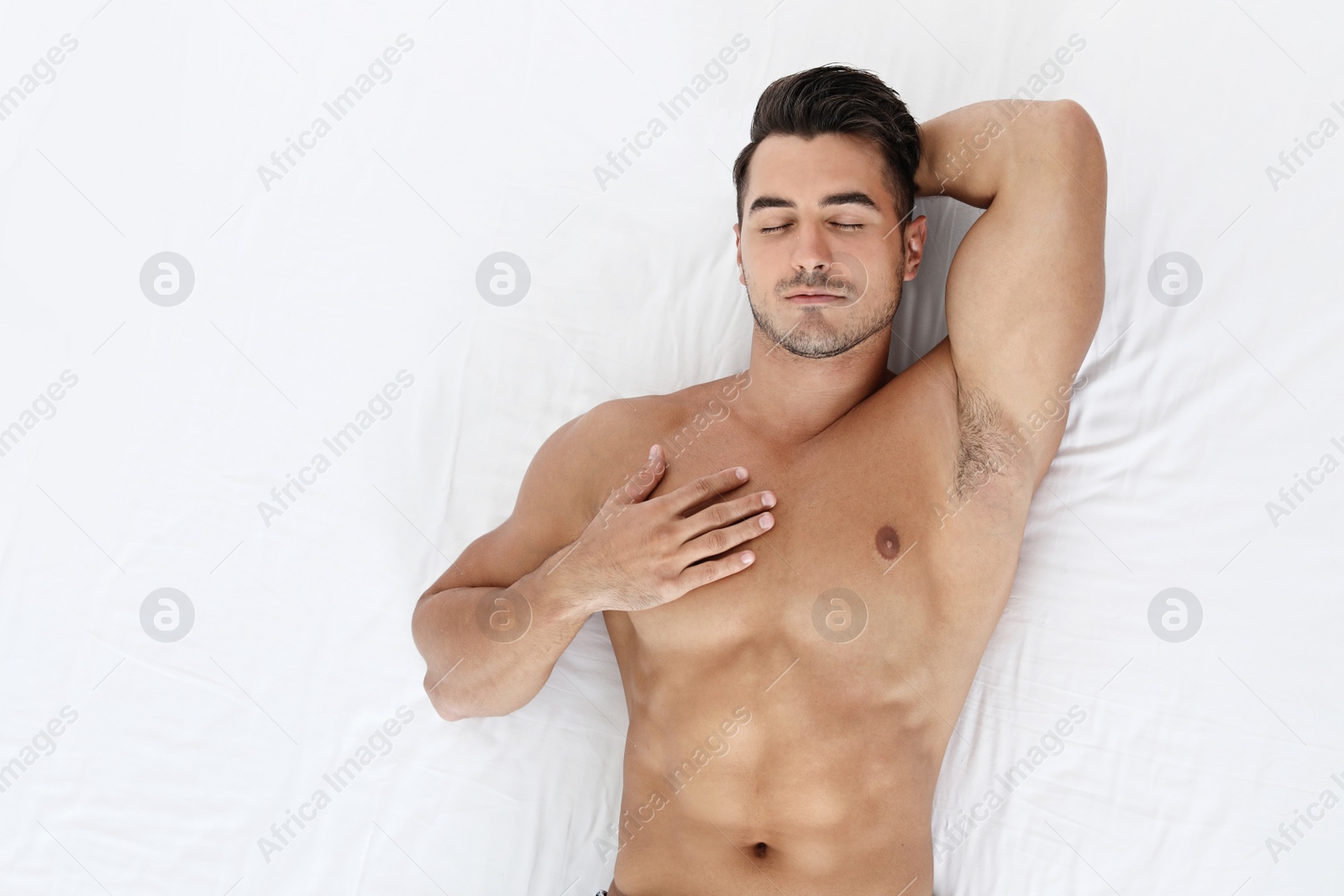 Photo of Sexy young man sleeping on soft bed, top view