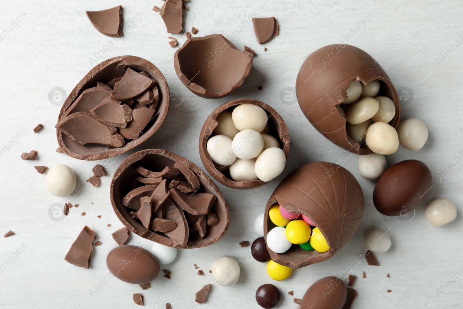 Photo of Broken chocolate eggs with candies on white wooden table, flat lay