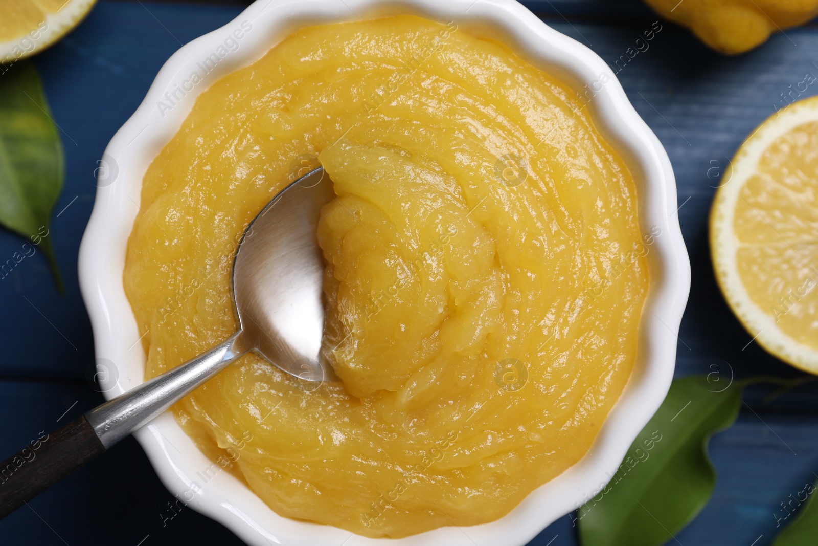 Photo of Delicious lemon curd in bowl and spoon on blue table, top view