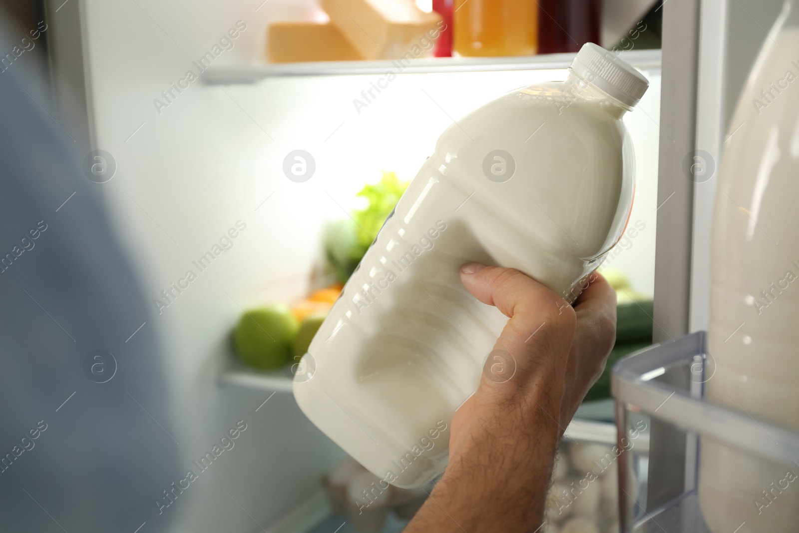 Photo of Man with gallon of milk near refrigerator indoors, closeup