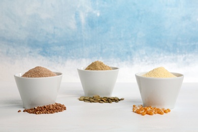 Bowls with different types of flour and seeds on table against color background. Space for text