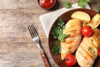 Fried chicken breasts served with sauce and garnish on wooden background, top view. Space for text