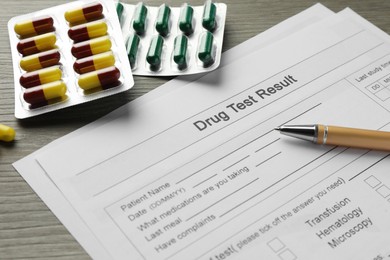 Photo of Drug test result form, pills and pen on wooden table, closeup