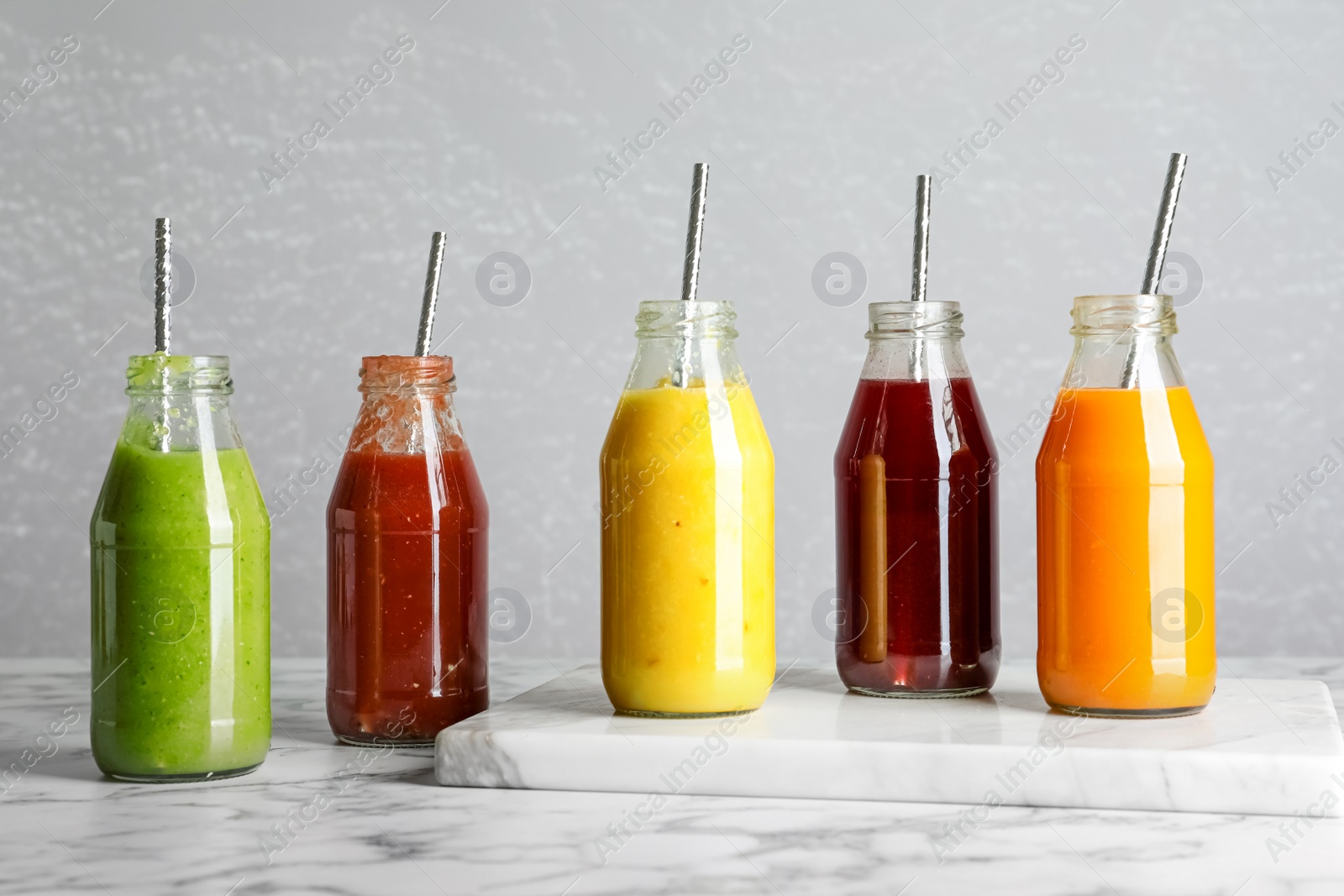 Photo of Bottles of delicious juices on white marble table