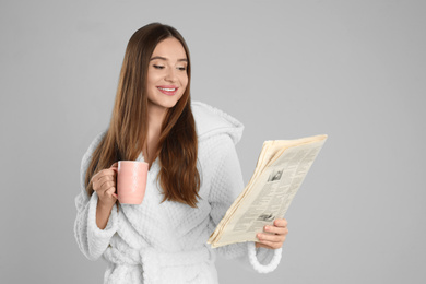 Photo of Beautiful young woman in bathrobe reading newspaper on light grey background
