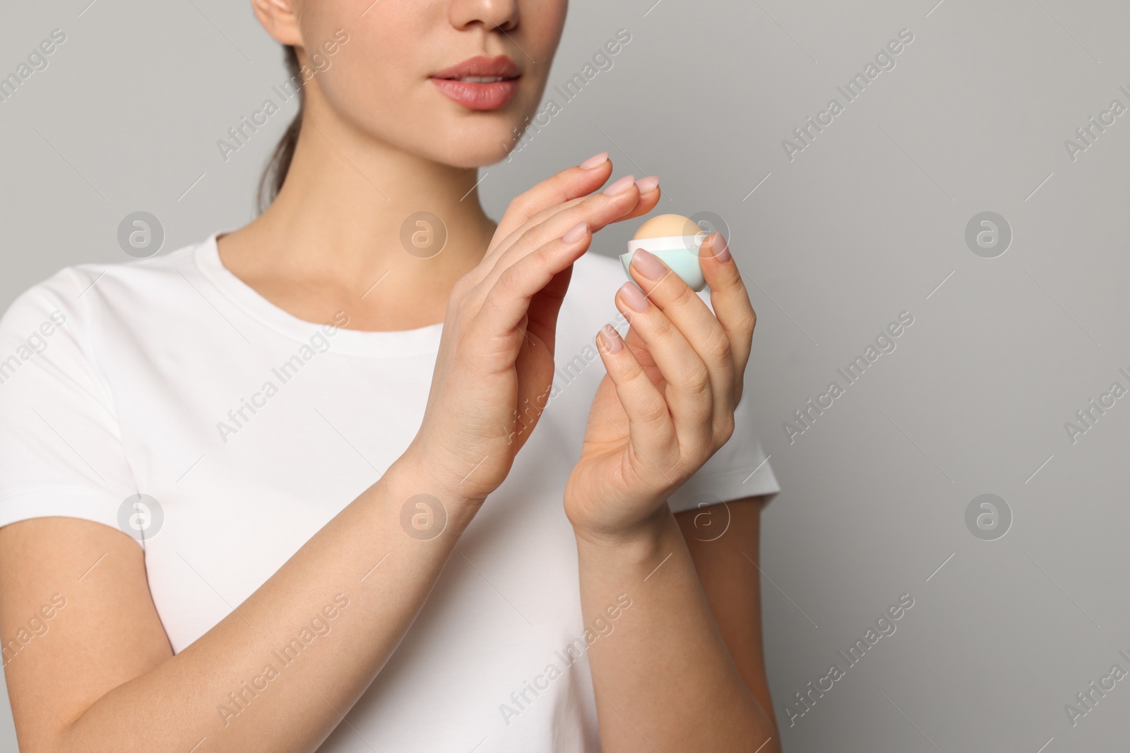 Photo of Young woman with lip balm on grey background, closeup