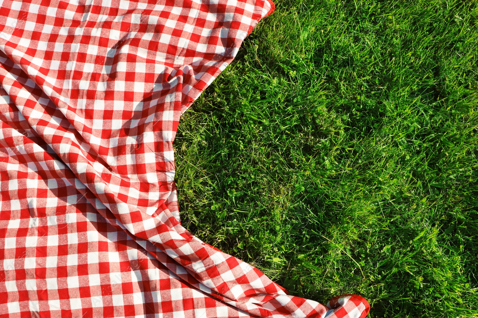 Photo of Checkered picnic tablecloth on fresh green grass, top view. Space for text